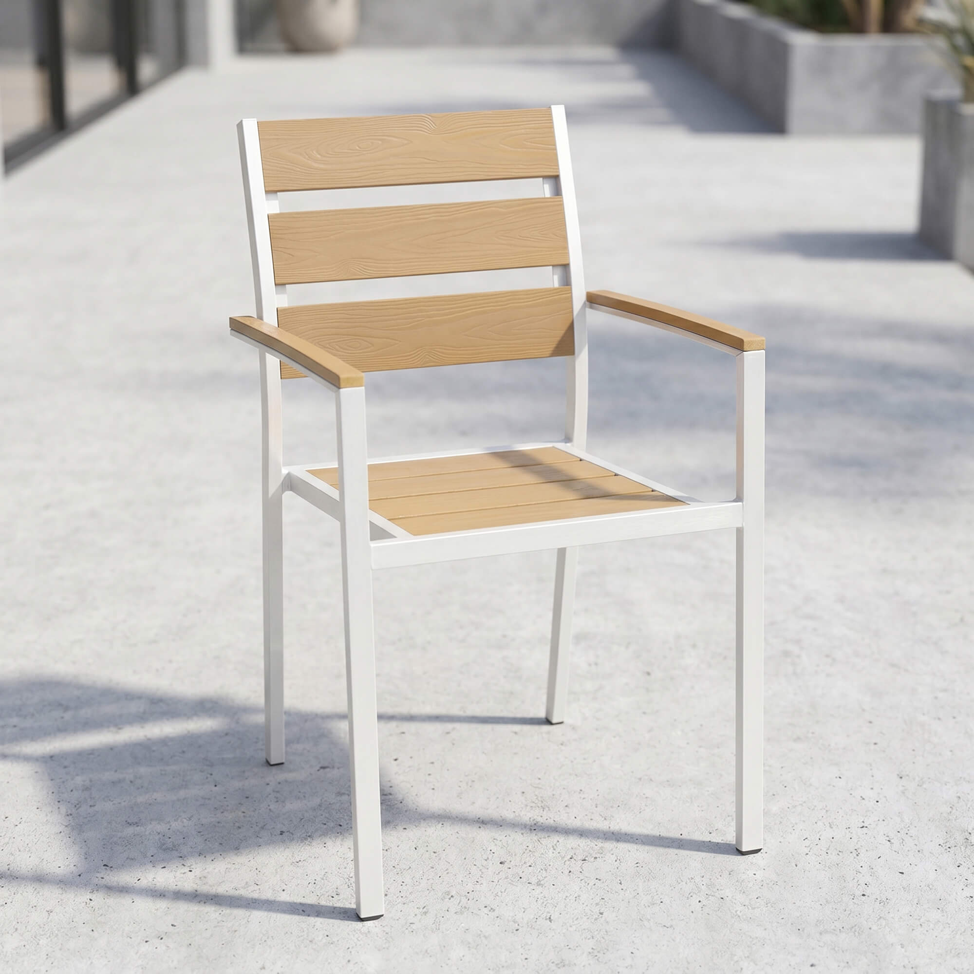 Stapelbarer Outdoorstuhl in Teak mit Armlehnen auf gepflasterter Terrasse