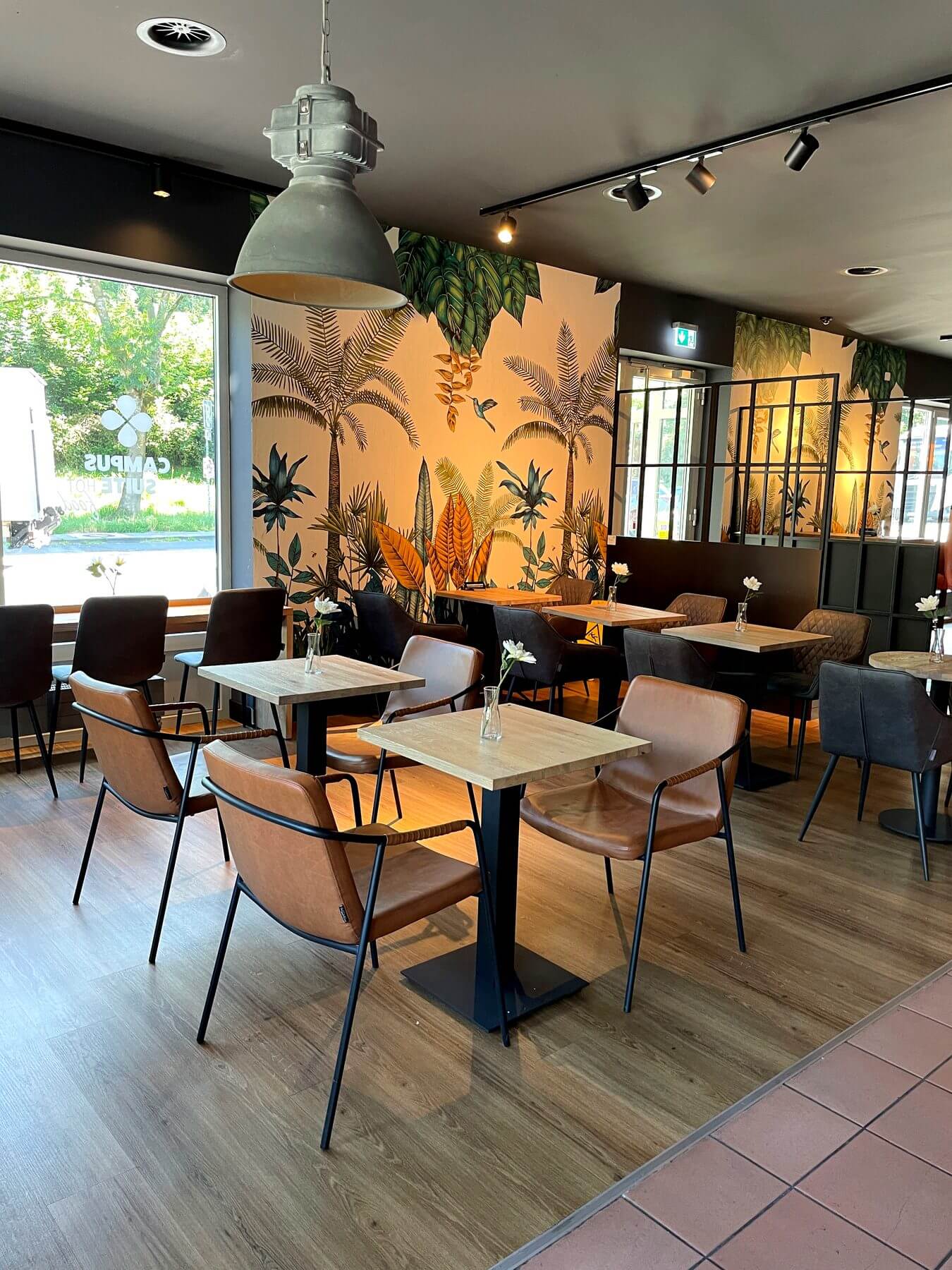 Sitzbereich bei Coffee Fellows Campus Suite mit kompakten Tischen, Stühlen und dekorativer Wandgestaltung