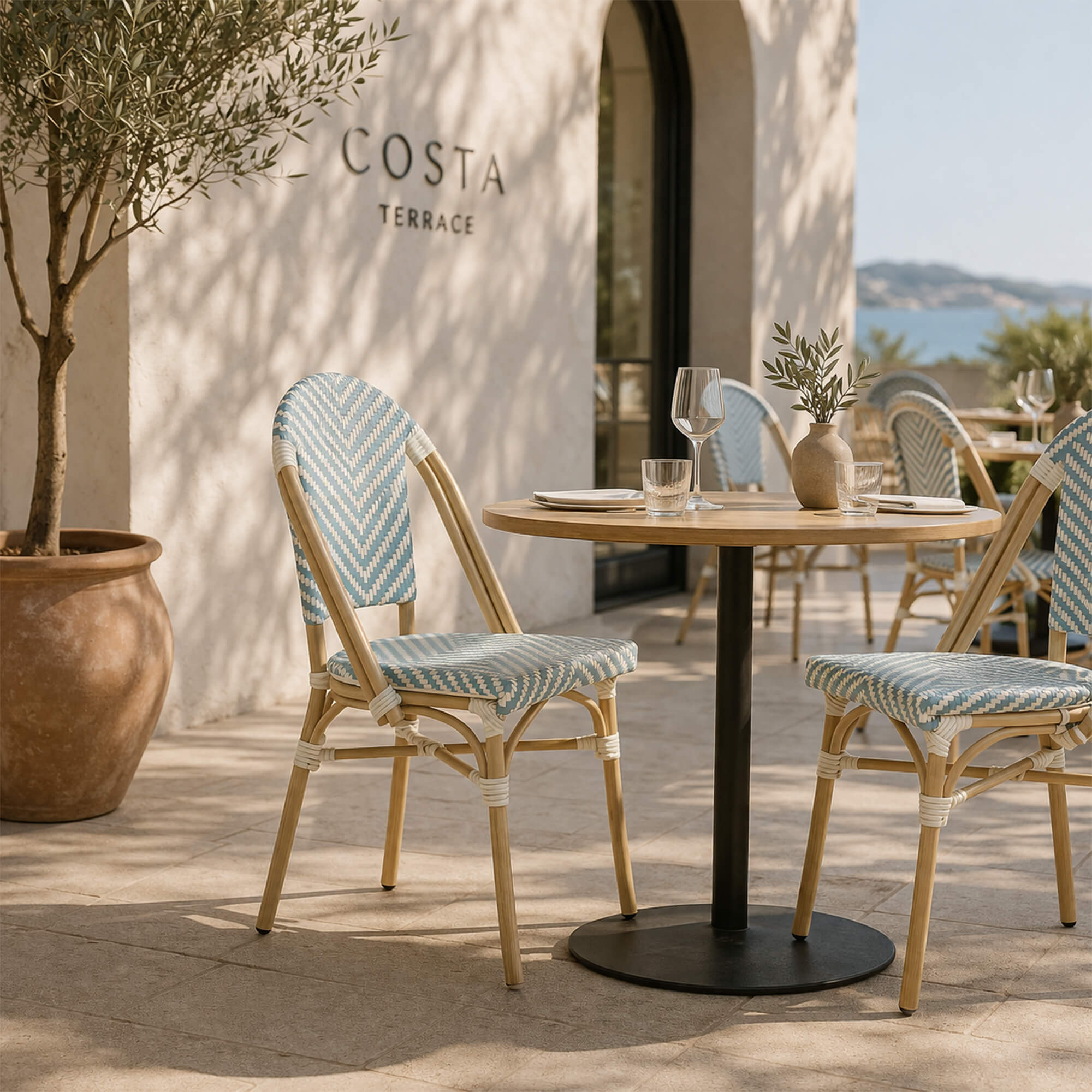 Outdoorstuhl Zypern – blau-weißer Bistrostuhl in Flechtoptik auf stilvoller Holzterrasse mit Blumen
