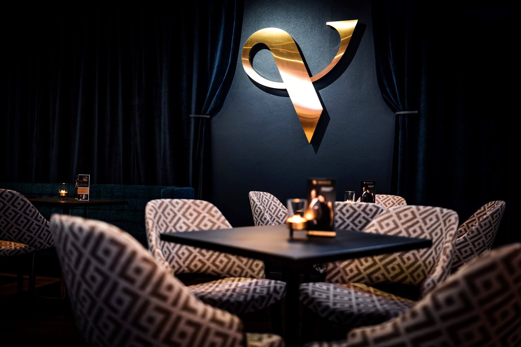 Sitzgruppe im Zaubertheater VERSCHMITTST vor dunklem Vorhang und goldenem Wandlogo