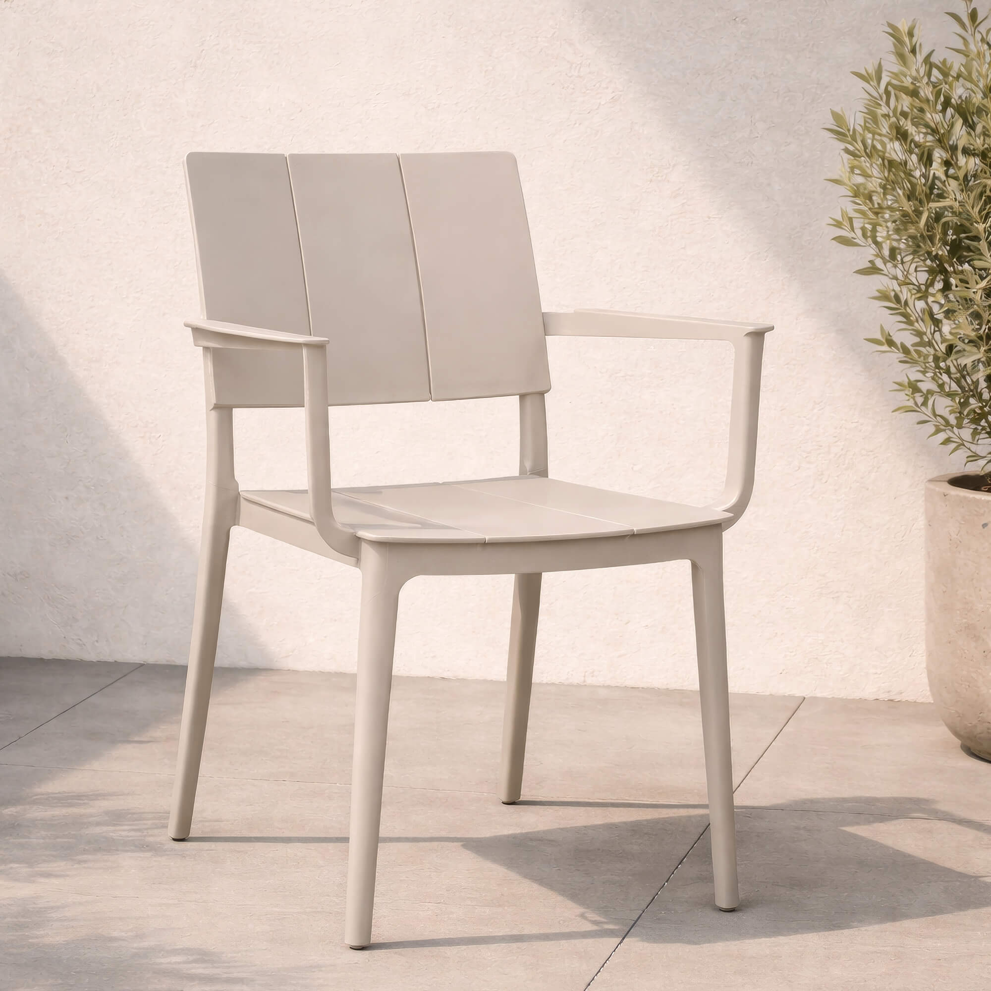 Outdoor Kunststoffstuhl Foma in Light Grey mit Armlehnen auf heller Terrasse vor strukturierter Wand