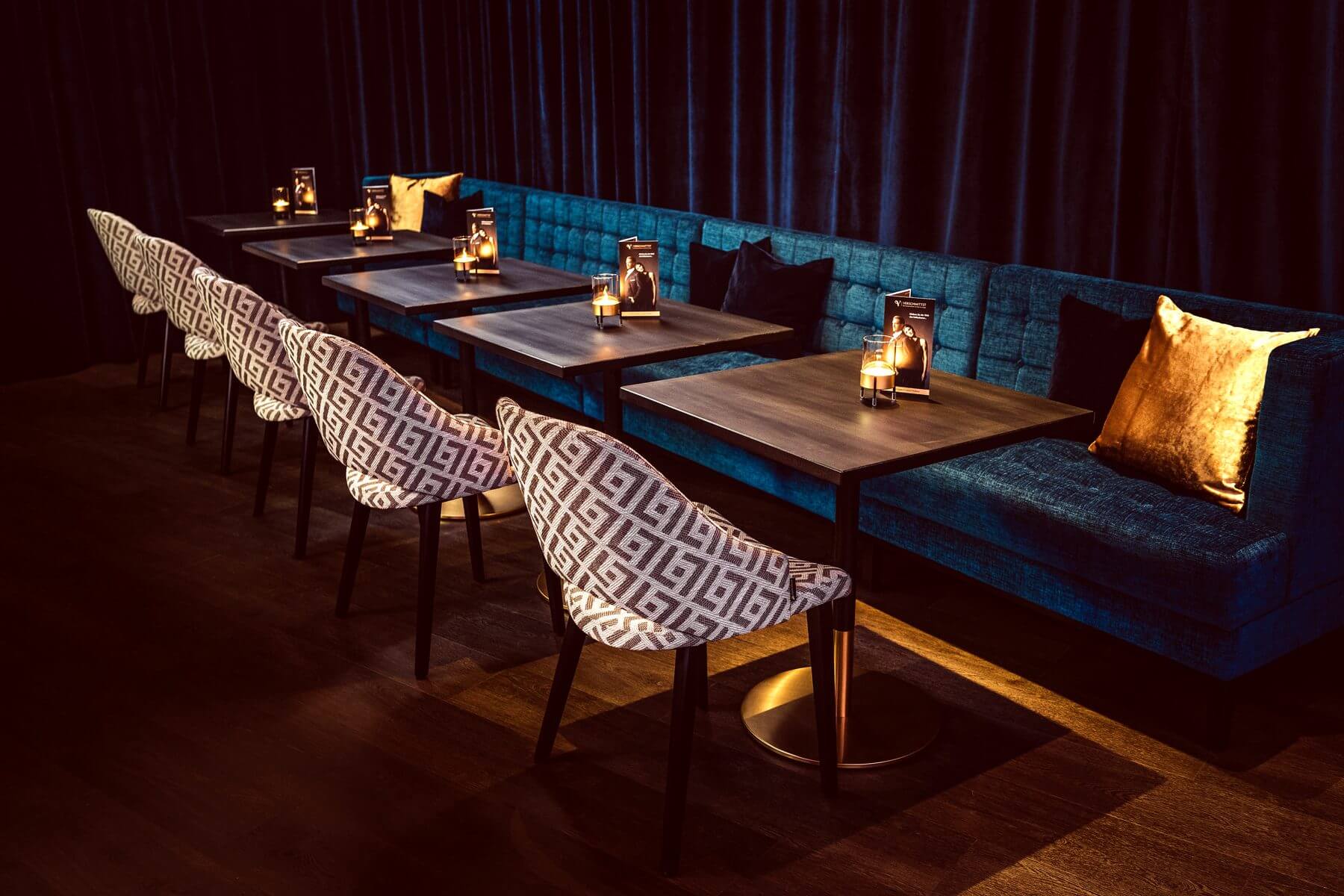 Lange Sitzreihe in der Bar & Lounge von VERSCHMITTST mit gemusterten Cizron-Stühlen und blauer Polsterbank