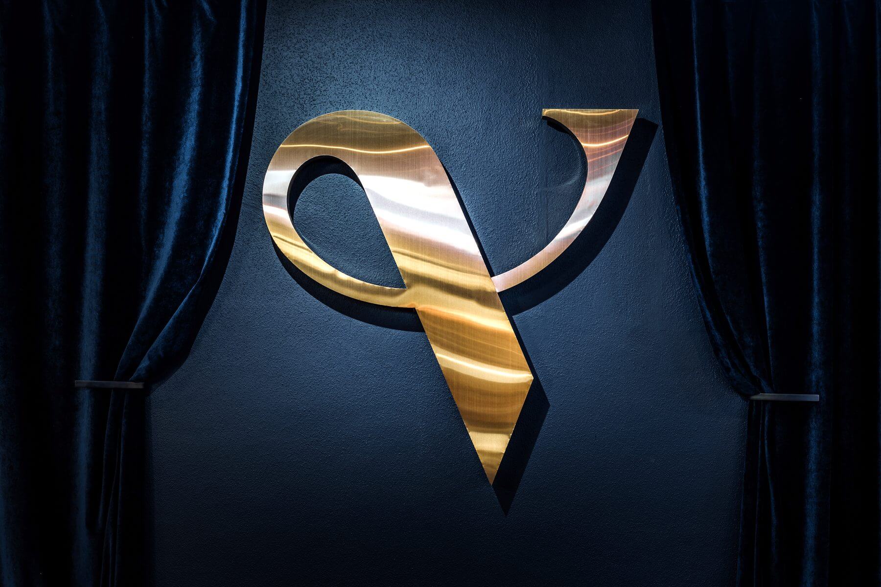 Wanddetail in der Bar & Lounge des Zaubertheaters VERSCHMITTST mit goldenem Logo und dunklem Vorhang