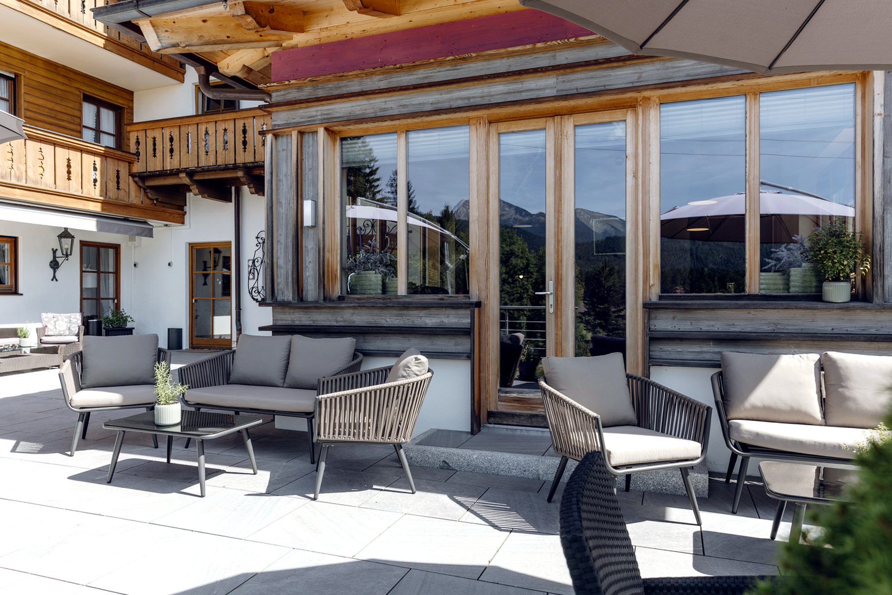 Loungebereich vor dem Esszimmer am Bichl mit Outdoor-Möbeln und großen Fenstern