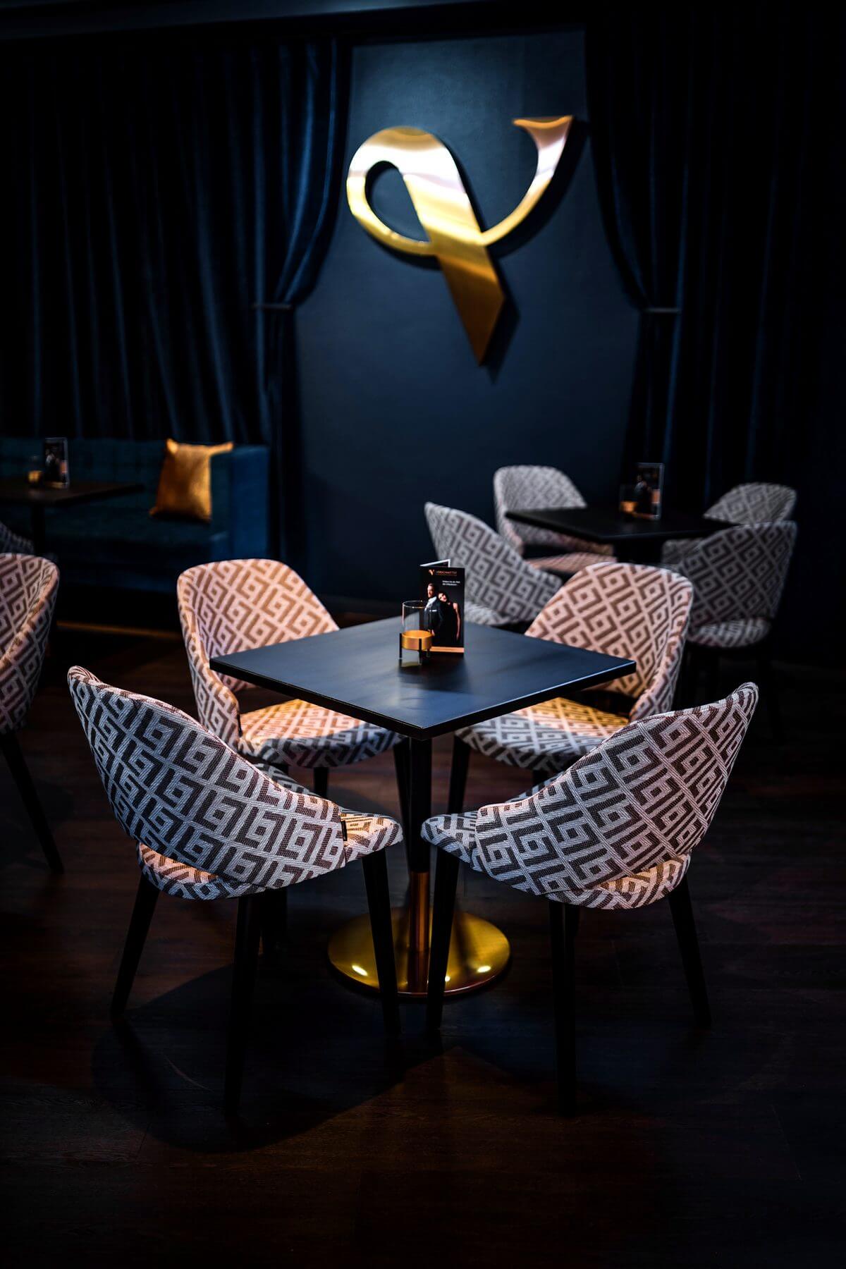 Hochformat einer Sitzgruppe in der Bar & Lounge von VERSCHMITTST mit Cizron-Stühlen und dunklem Wandvorhang